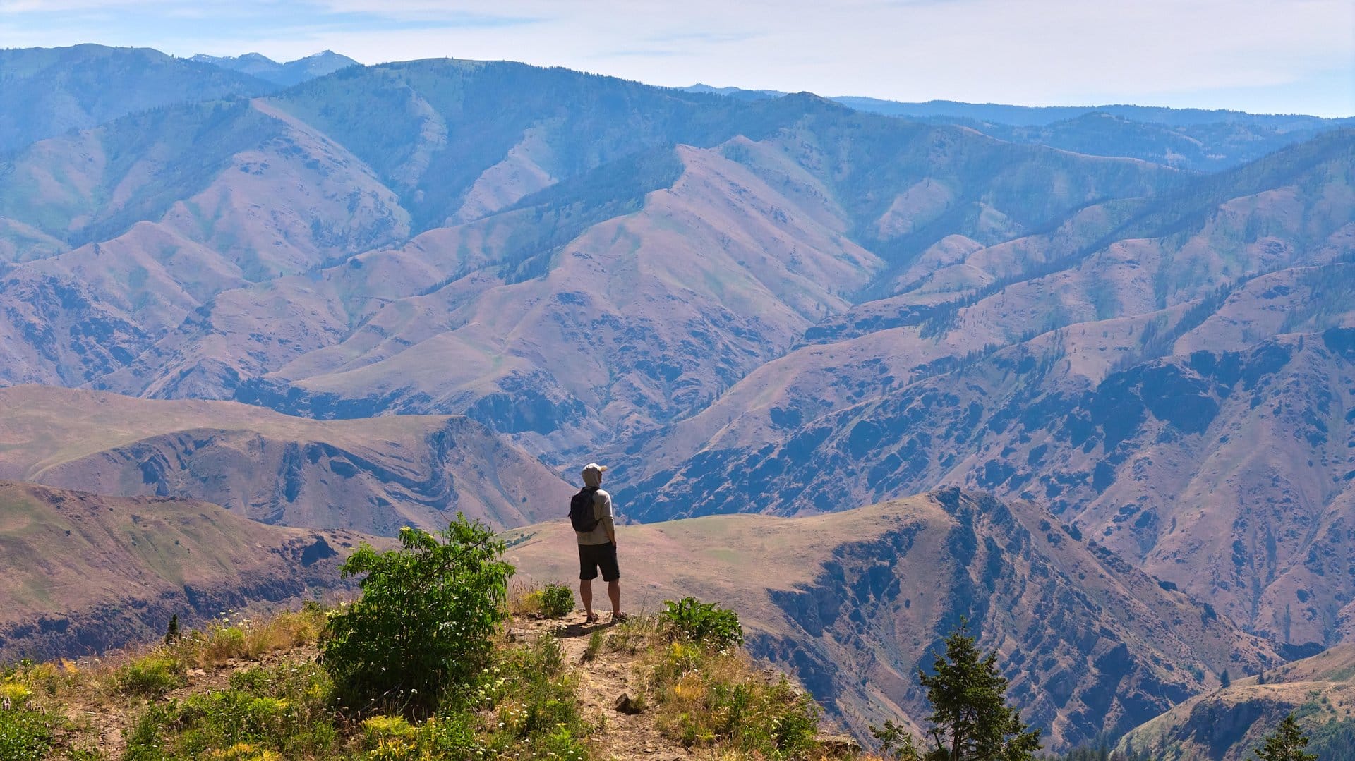 A person stands on a ridgeline overlooking the vast Hells Canyon.
